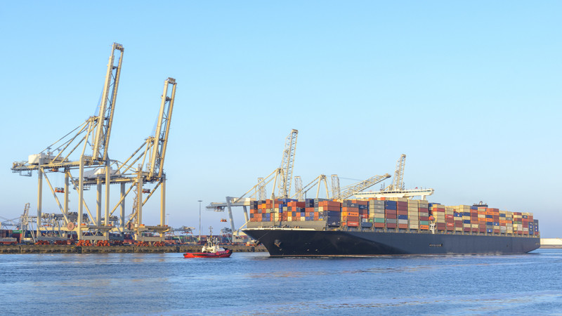 NYK Eagle cargo container ship  of Nippon Yusen Kabushiki Kaisha shipping company (or short NYK Line) leaving the port of Rotterdam in The Netherlands. Huge overhead cranes in the background are unloading containers from vessels and putting new containers with cargo on board.